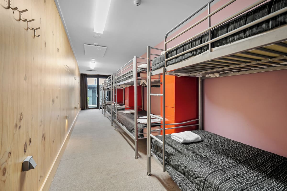 A dormitory with bunk beds, wooden walls, and a corridor leading to an exit.