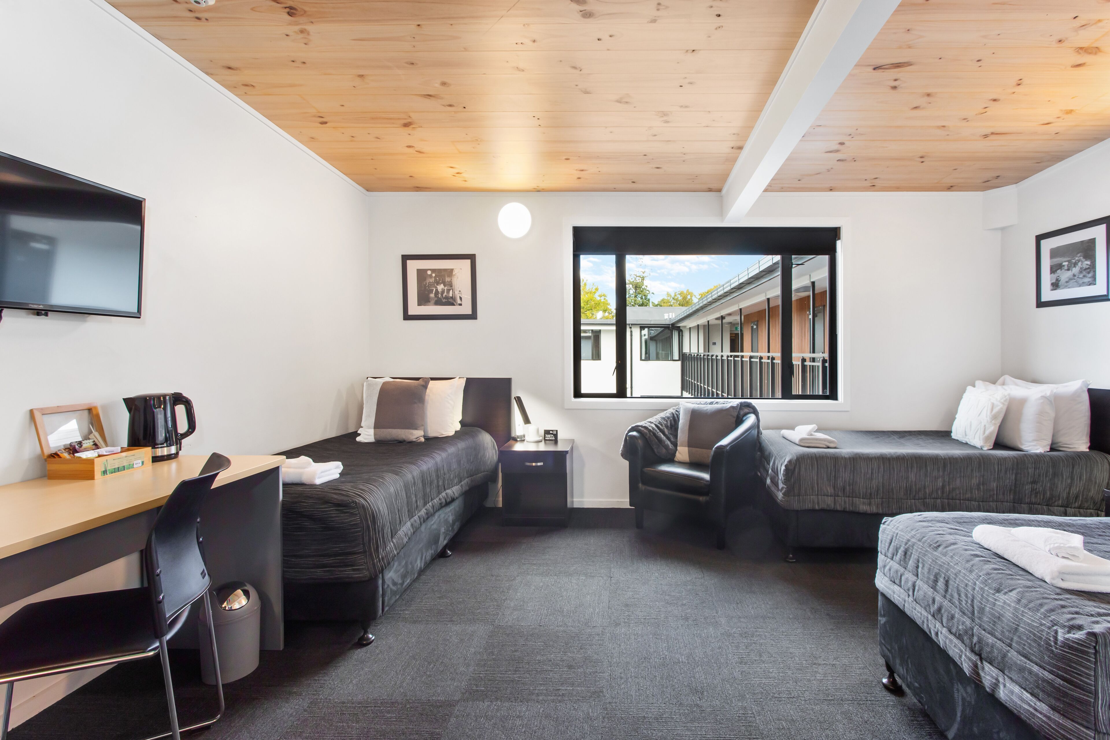 Een moderne hotelkamer met een houten plafond, een bureau, twee eenpersoonsbedden, een stoel en een groot raam met uitzicht.