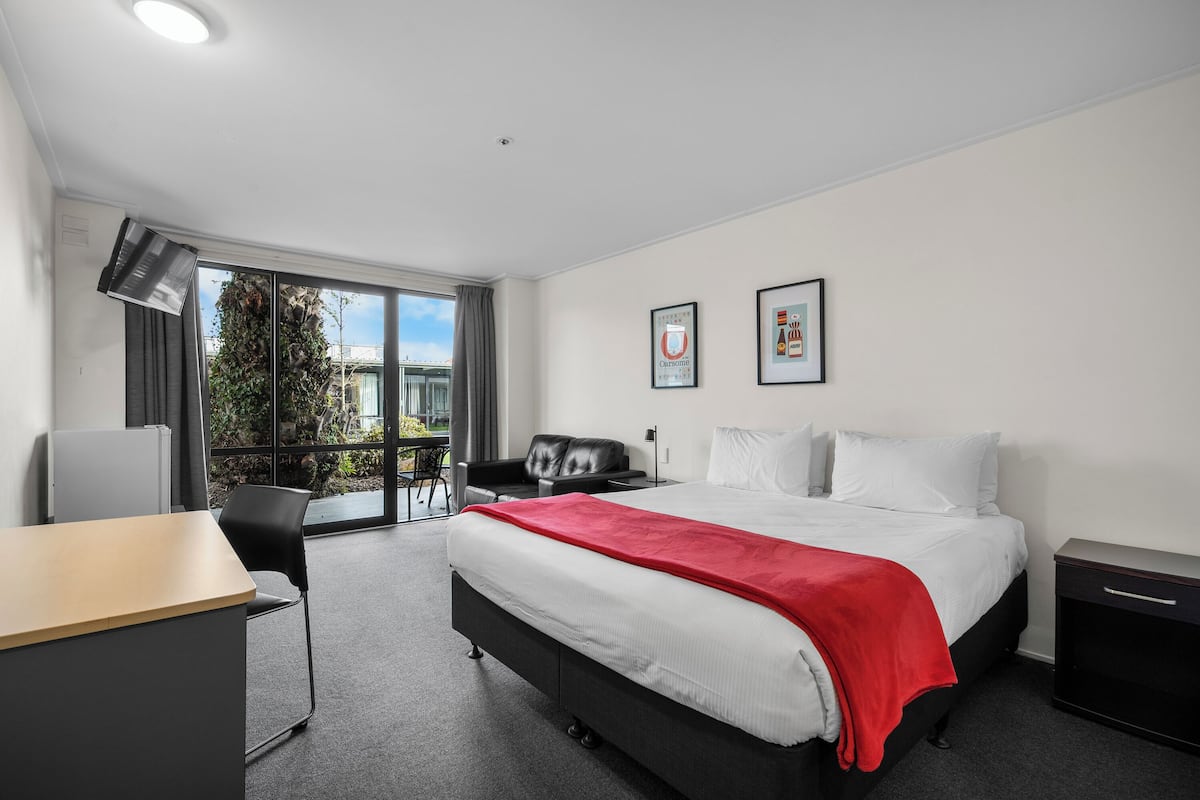A modern hotel room with a large bed, a desk, a chair, and a balcony with a view.