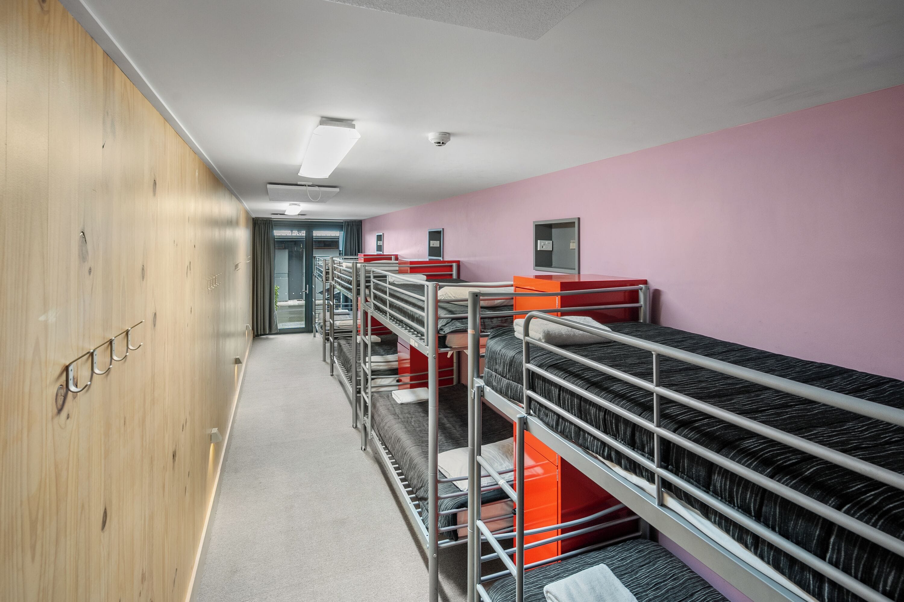 A corridor with bunk beds, wooden lockers, and a pink wall.