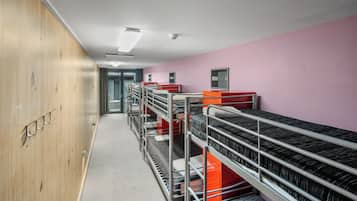 A corridor with bunk beds, wooden lockers, and a pink wall.
