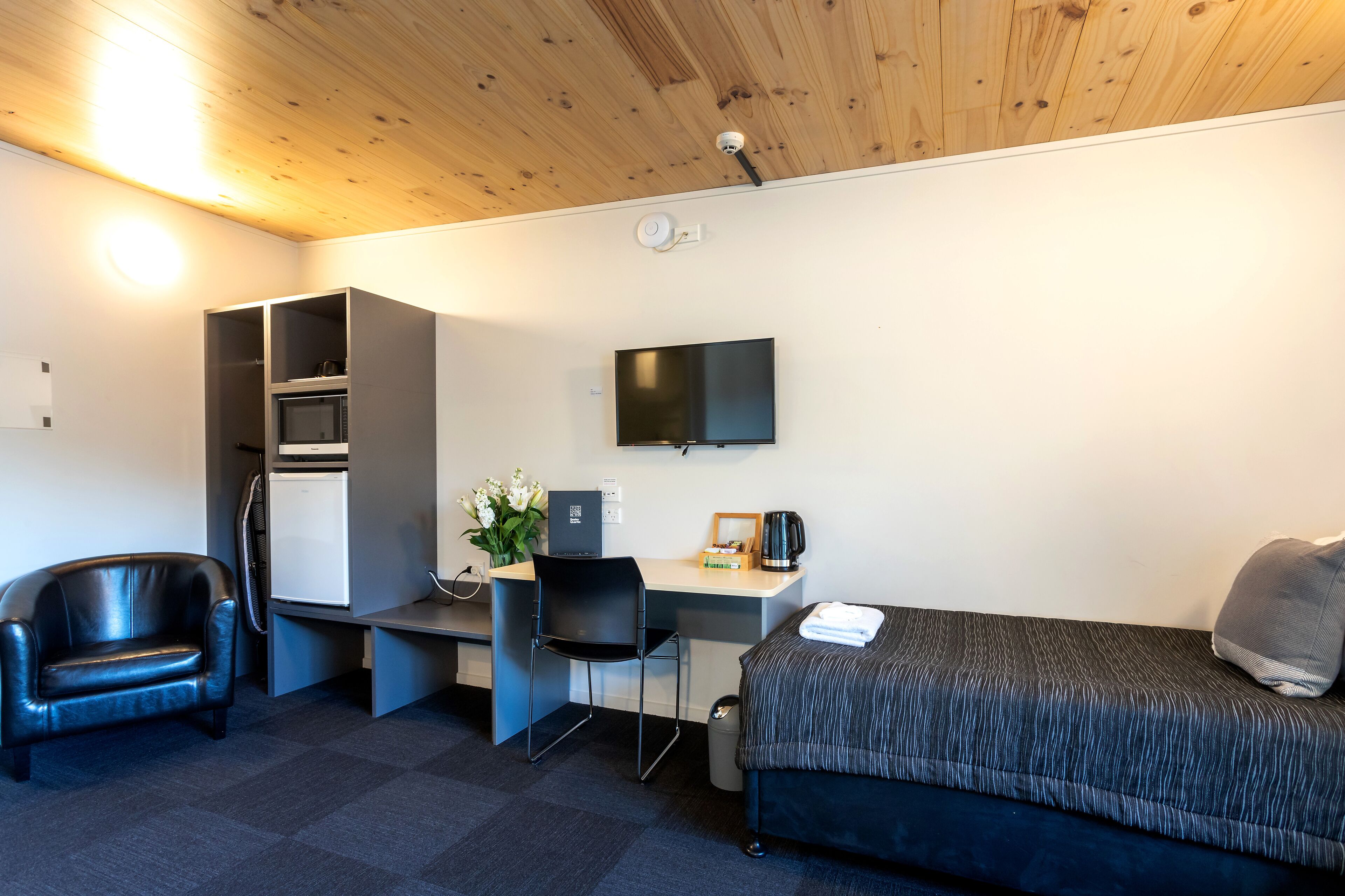 Une chambre d’hôtel compacte comprenant un lit, un bureau avec une chaise, une télévision et une petite kitchenette.