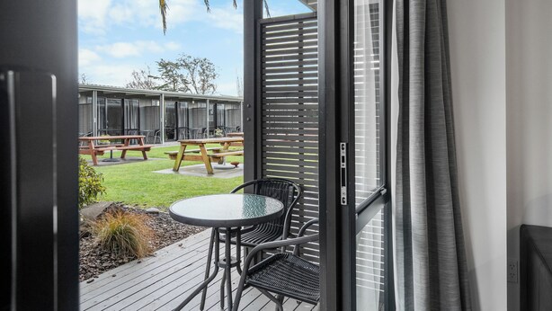 A balcony with a table and chairs, overlooking a grassy area with picnic tables and a building in the background. - Bealey Quarter (Christchurch)