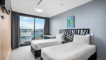 Una habitación de hotel con dos camas, un escritorio y un amplio ventanal con vista a un puente.