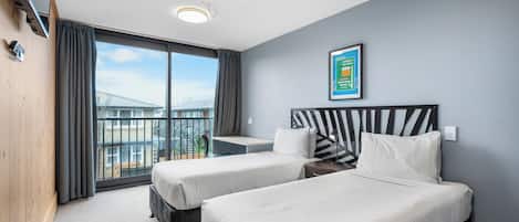 Una habitación de hotel con dos camas, un escritorio y un amplio ventanal con vista a un puente.