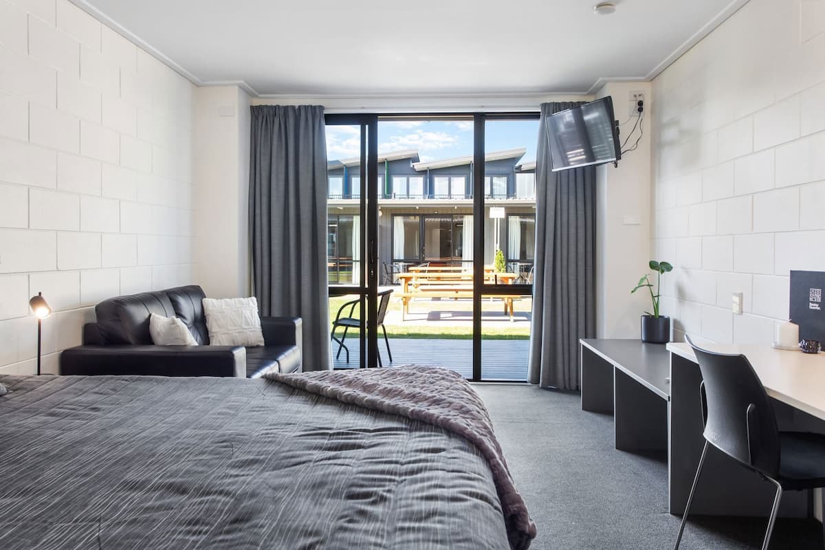 A modern hotel room with a large bed, a desk, a chair, and a TV.