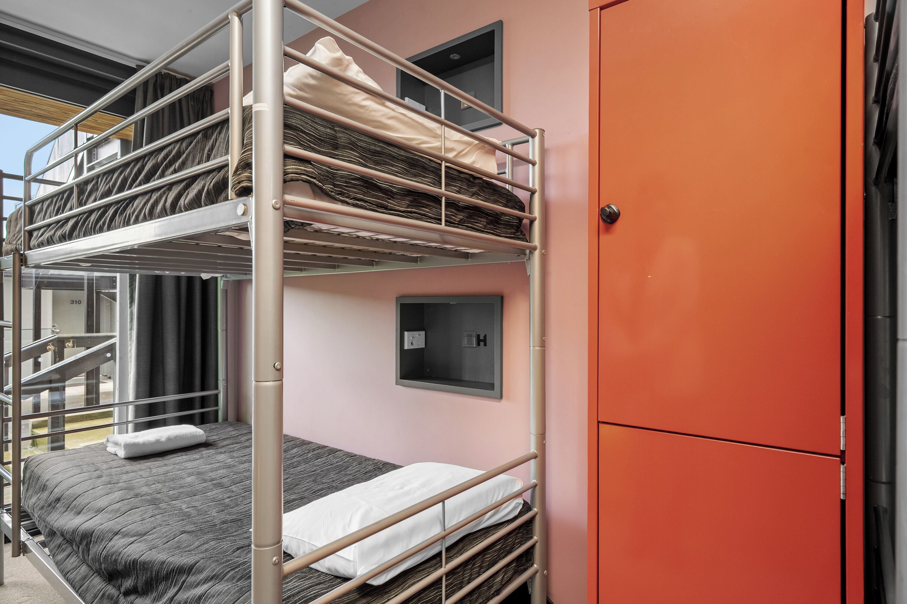 A bunk bed room with a metal frame, a red cabinet, and a window with curtains.