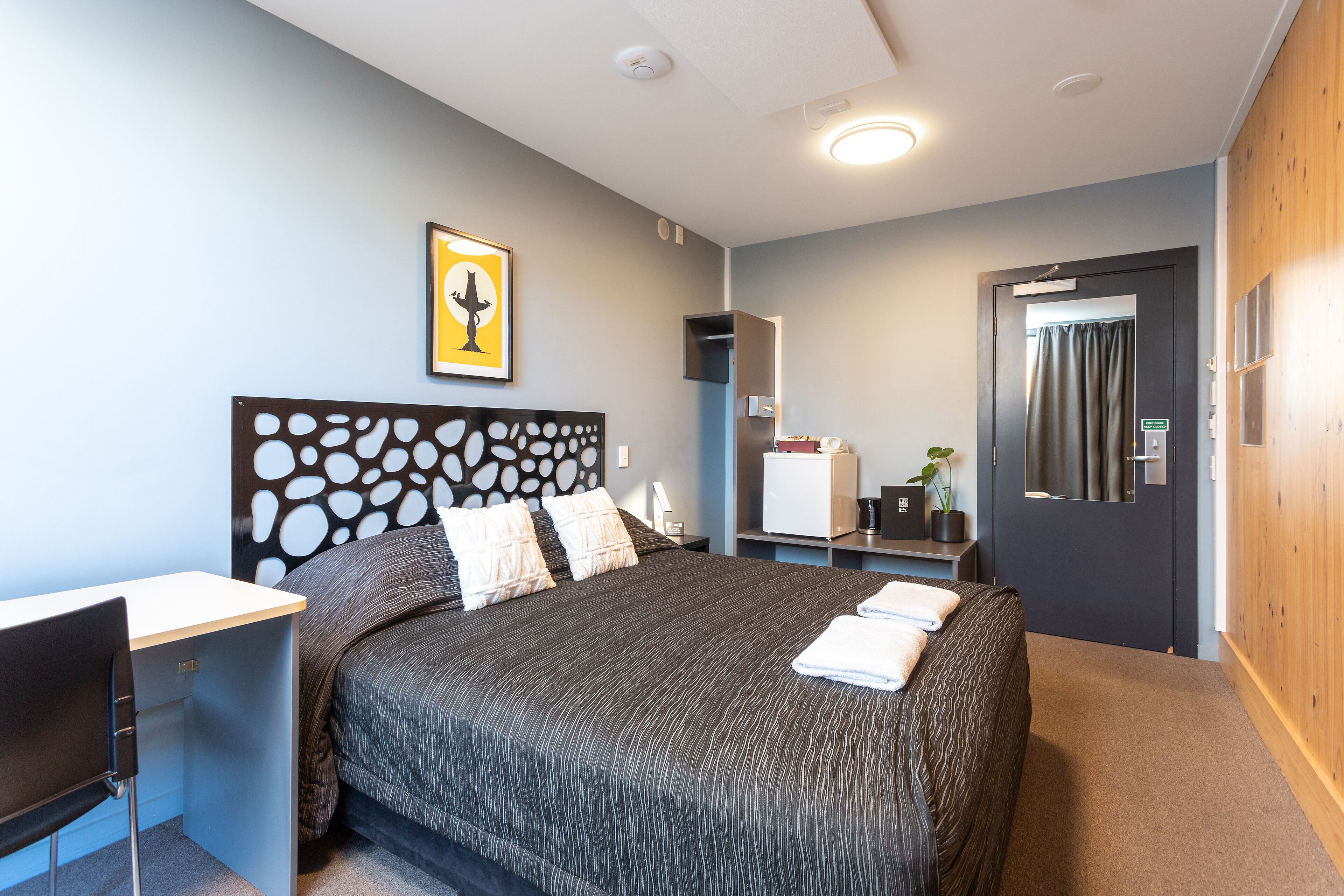 A modern hotel room with a bed, desk, and wardrobe.
