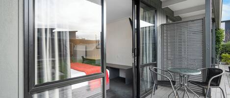 A balcony with a sliding glass door leading to a bedroom, a small table with chairs, and a view of the outside.
