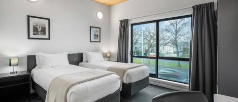A hotel room with two beds, a large window with curtains, a desk, and a chair.