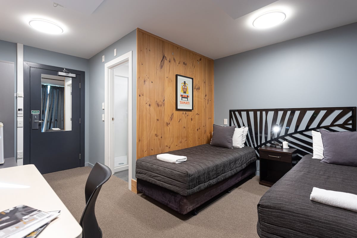 A modern hotel room with a wooden accent wall, a bed with a headboard, a desk, and a chair.