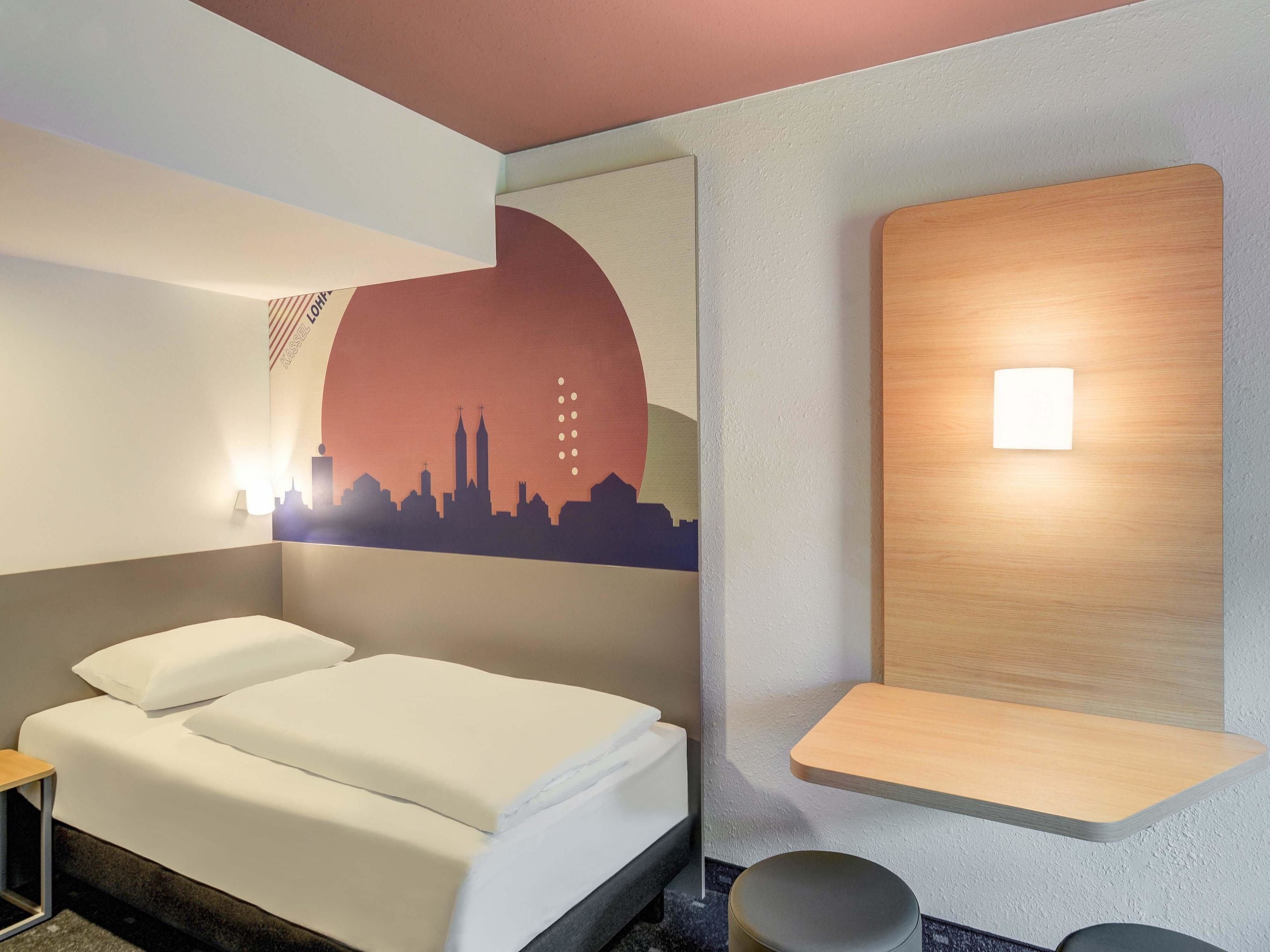 Ein Hotelzimmer mit einem Bett, einer Wandablage und einem Stadtbild-Wandgemälde.