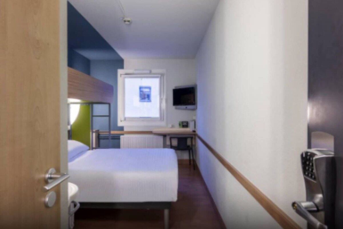 Une chambre d’hôtel avec un lit, un bureau, une chaise, une télévision et une fenêtre.