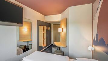 Habitación de hotel moderna con una cama grande, un espejo, una pequeña zona de estar y un televisor montado en la pared.