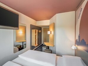 Une chambre d’hôtel moderne dotée d’un grand lit, d’un miroir, d’un petit coin salon et d’un téléviseur fixé au mur.