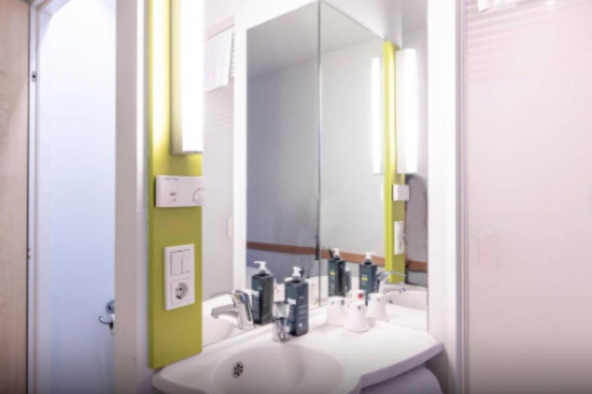 Une salle de bain avec un lavabo blanc, un miroir et des articles de toilette posés sur le comptoir.