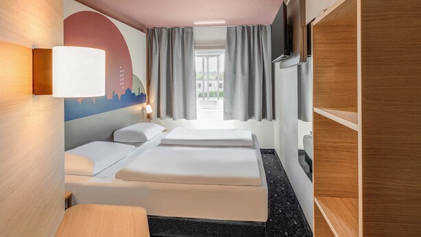 A hotel room with a bed, a desk, a TV, and a window with curtains. - B&B HOTEL Kassel-Lohfelden (Lohfelden)