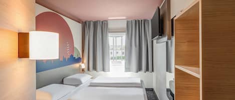 Ett hotellrum med en säng, ett skrivbord, en tv och ett fönster med gardiner.