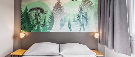 Habitación de hotel con una cama, dos mesitas de noche, una obra de arte en la pared con escena de bosque y una ventana con cortinas.