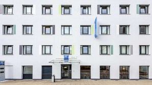 Un edificio moderno con múltiples ventanas, una entrada central y un letrero que dice 'ibis Budget'.