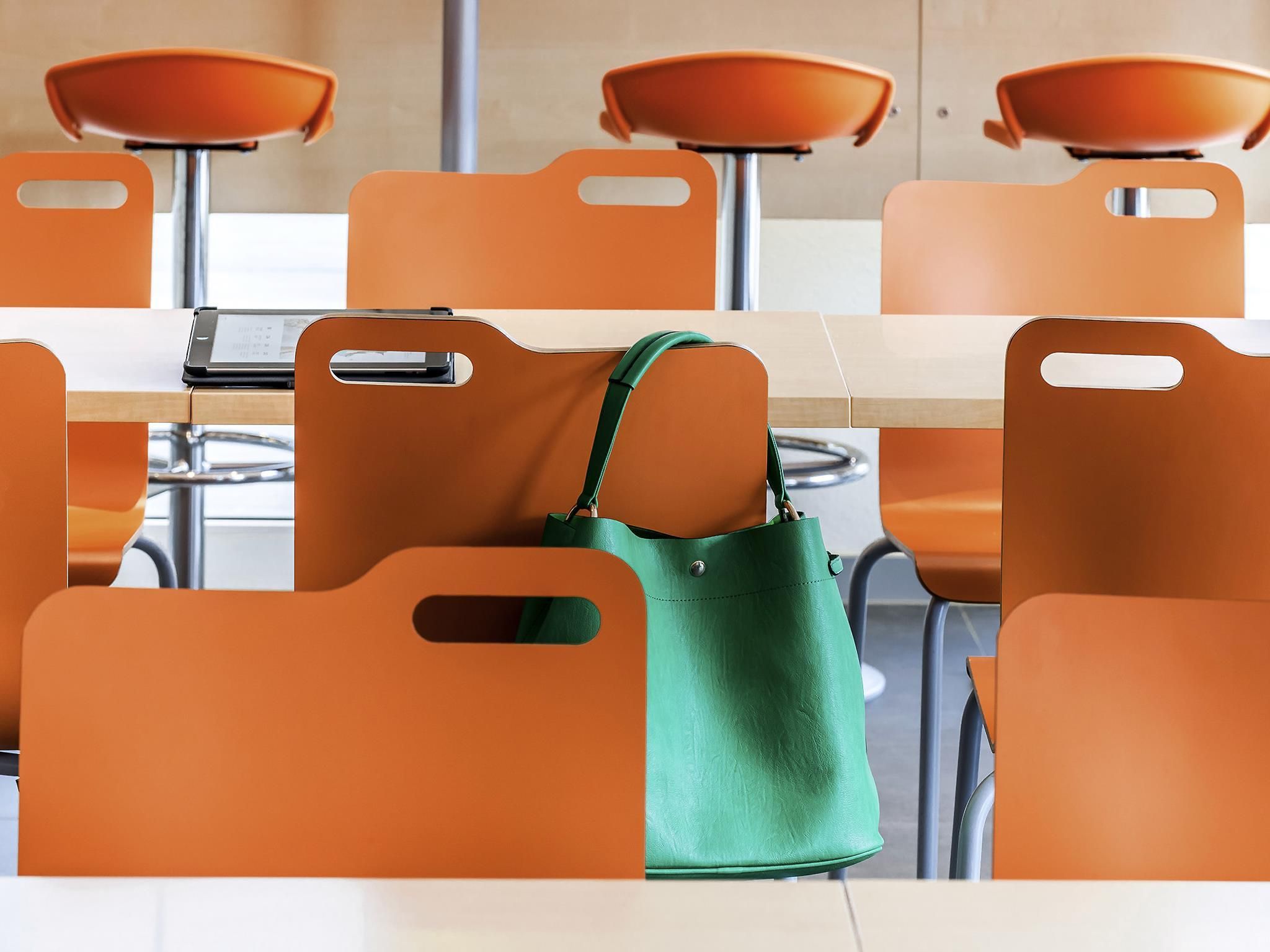 Un espace repas moderne avec des chaises orange et un sac à main vert posé sur l’une d’elles.