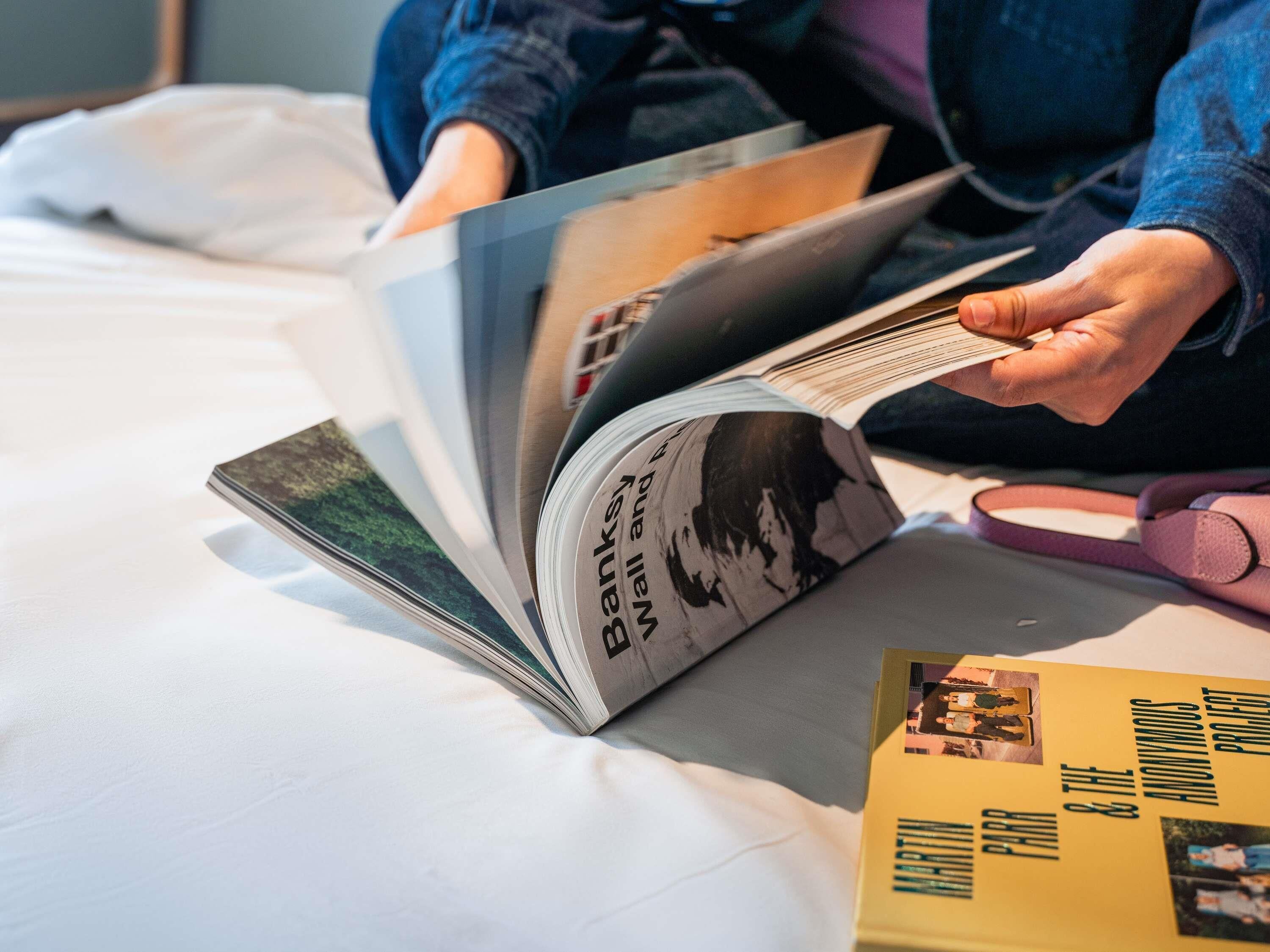 Une personne est assise sur un lit, un livre à la main, avec un oreiller et une couverture à proximité.