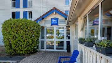 A building with a blue awning, a sign reading "ibis budget," and a row of potted plants along the side.