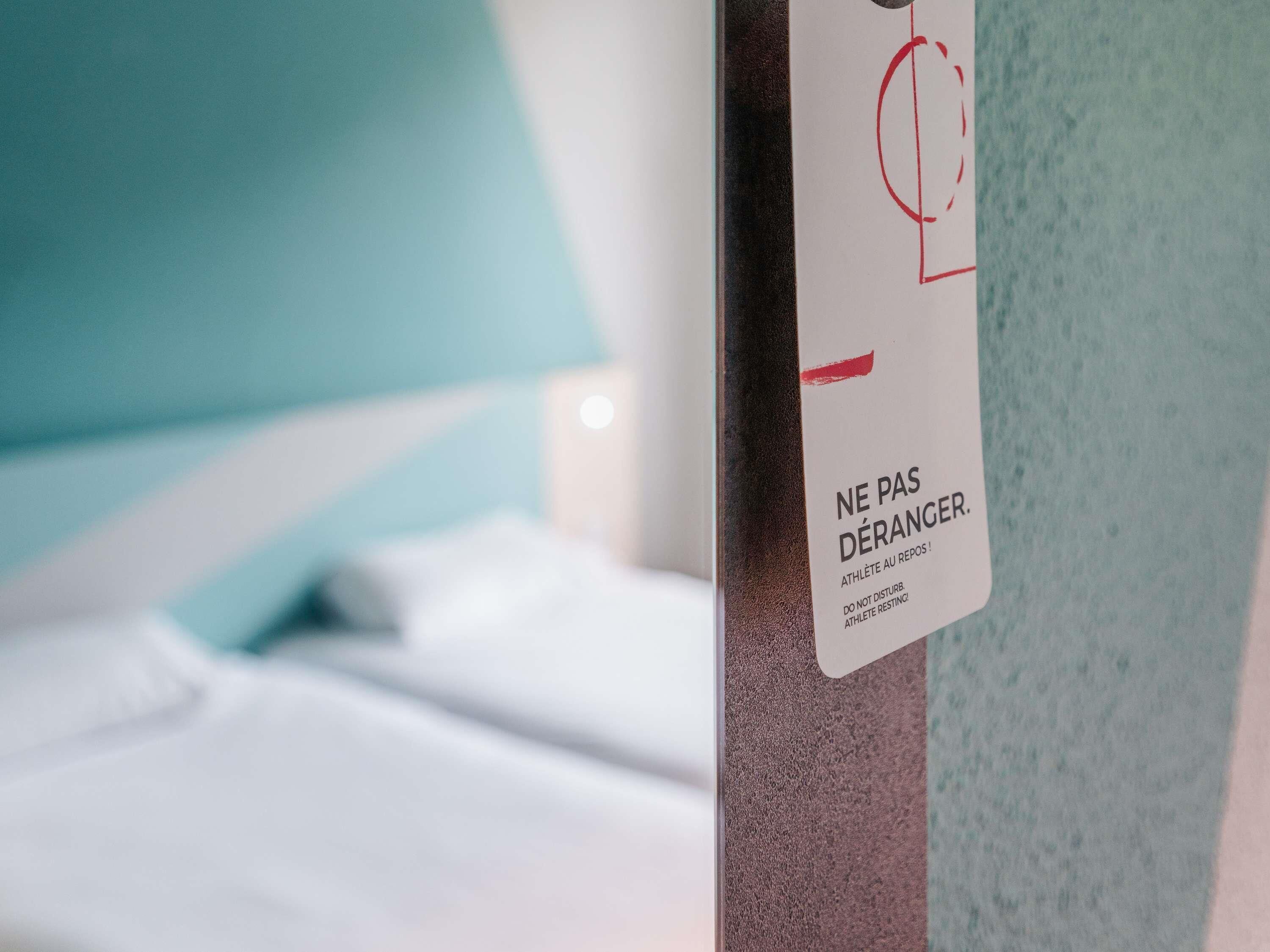 A close-up of a wall with a sign that reads 'NE PAS DÉRANGER. ATHLÈTE AU REPOS! DO NOT DISTURB. ATHLÈTE RESTING!'