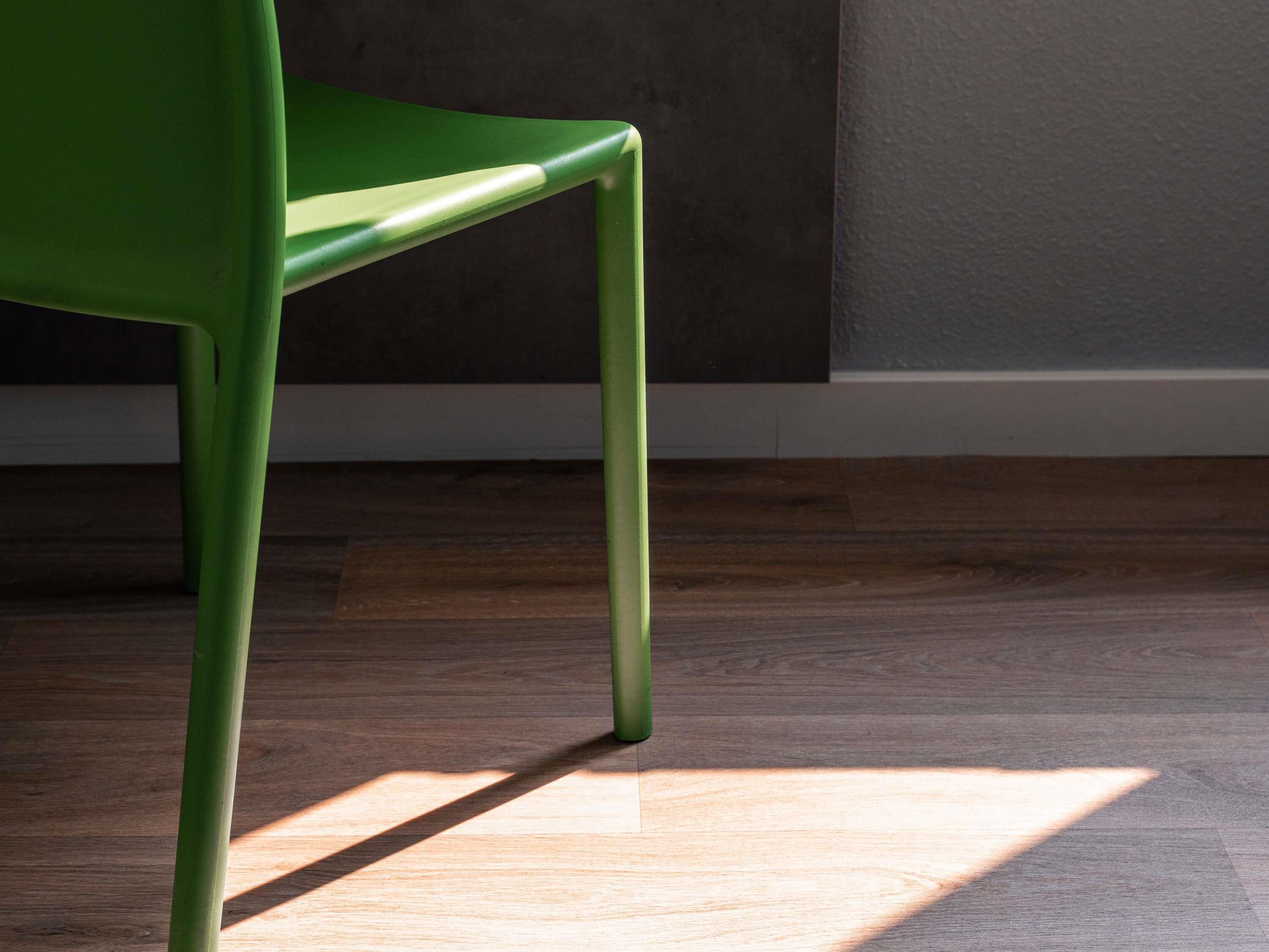 Una silla verde con respaldo recto y cuatro patas, sobre un piso de madera con una sombra proyectada.