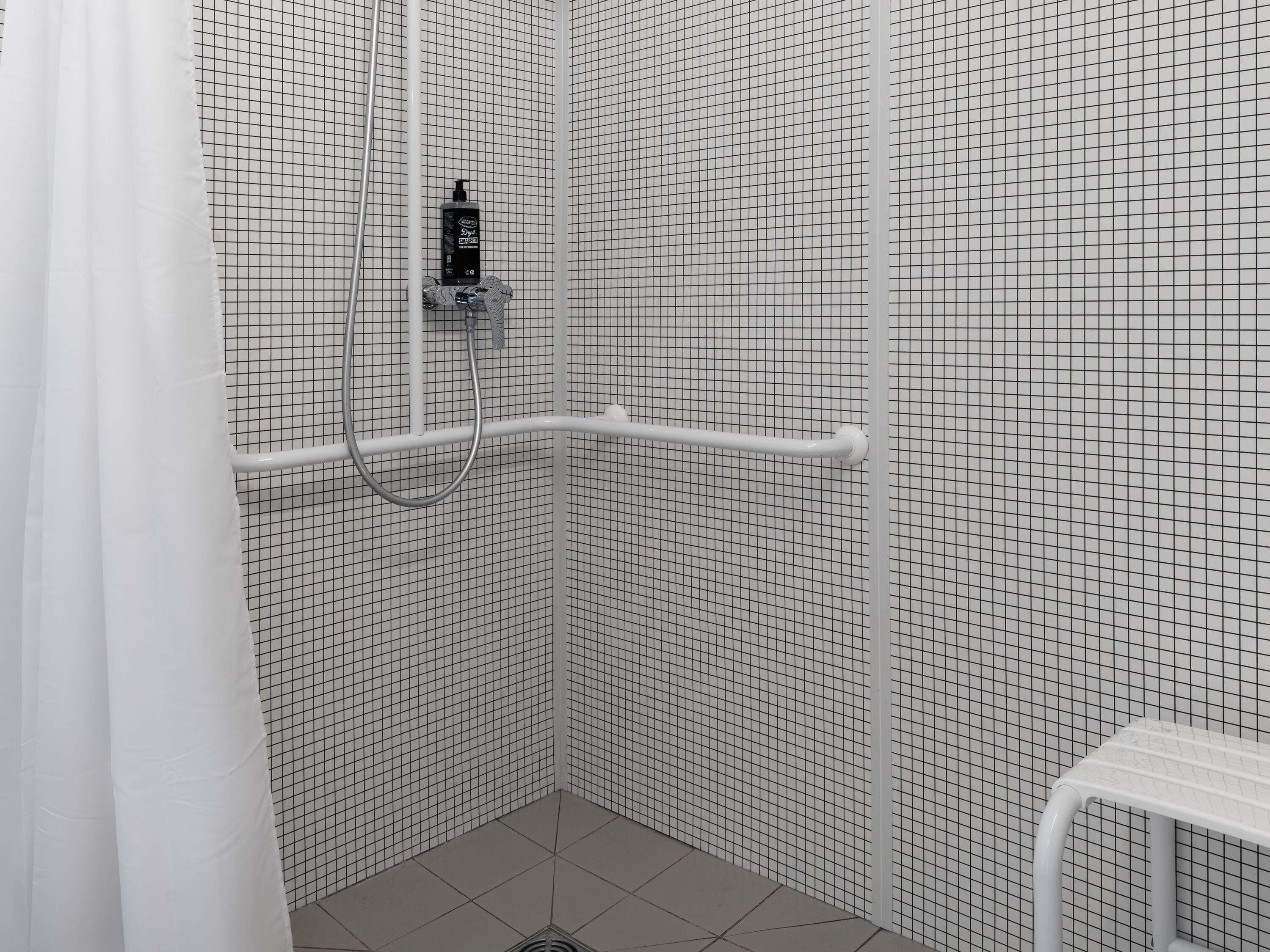 Eine Dusche mit einer Wand mit Gittermuster, einer weißen Haltestange und einem Duschkopf.