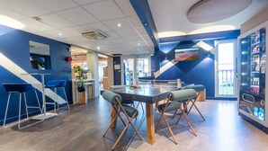Un espacio interior moderno con una mesa de ping pong, taburetes de bar y una máquina expendedora.