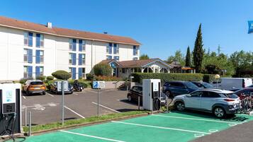 A parking area with electric vehicle charging stations, a building with a tiled roof, and a clear blue sky.