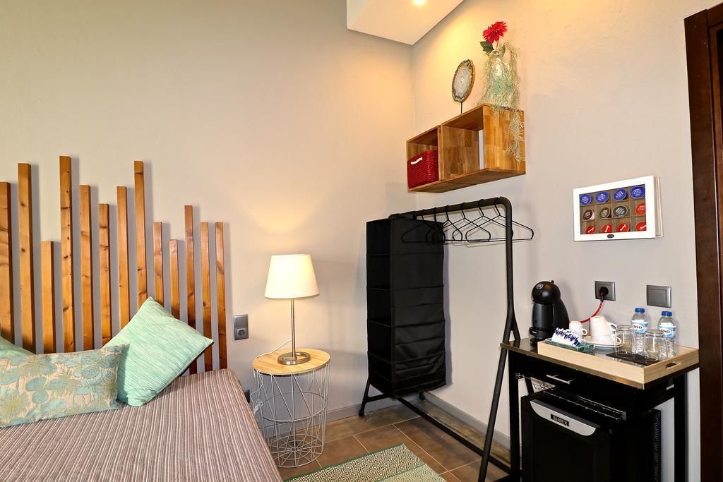 Hotellihuone, jossa on sänky, lamppu, kahvinkeitin ja pieni pöytä, jonka päällä on vesipulloja.