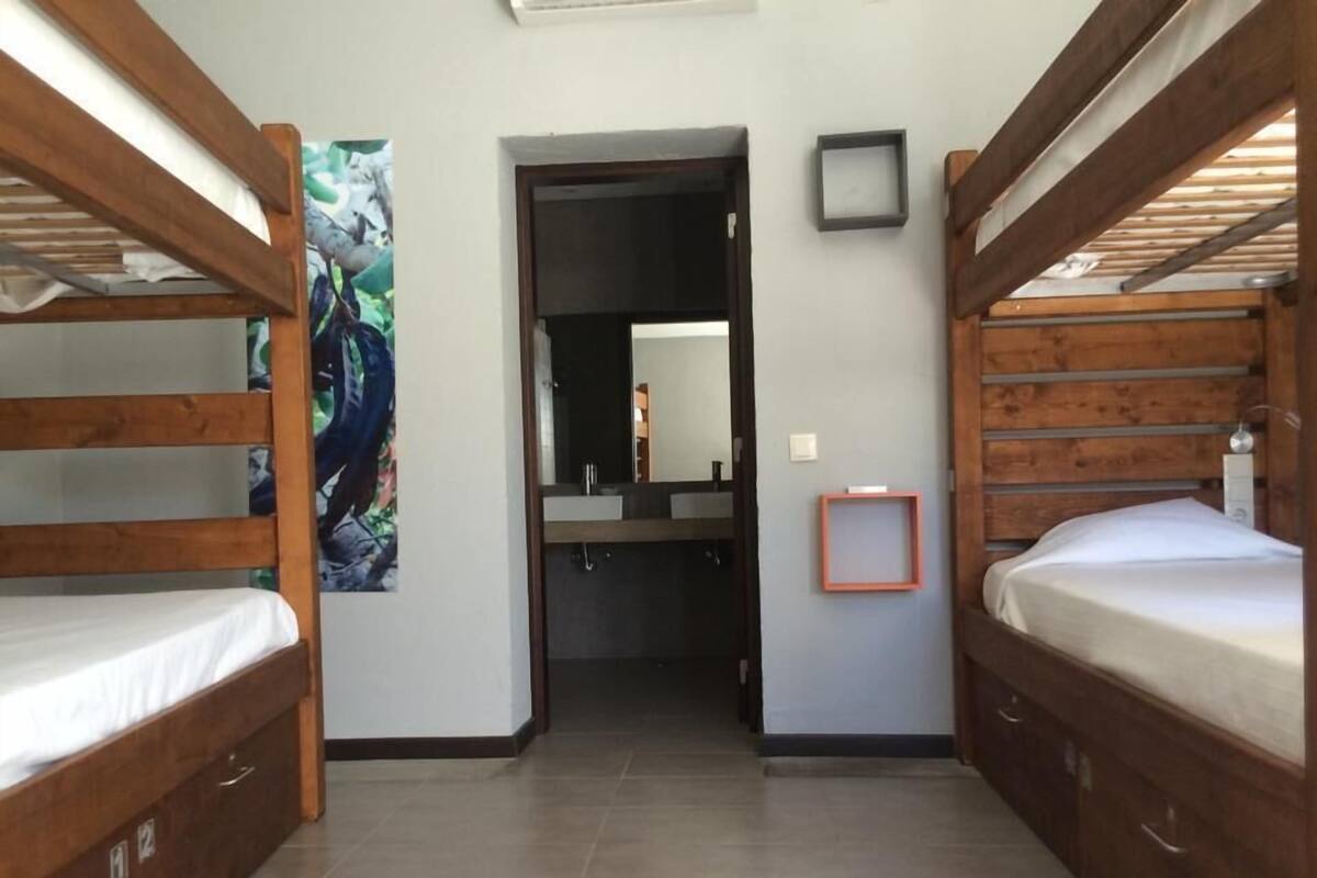 A compact room with two bunk beds, a small bathroom with a mirror, and a framed picture on the wall.