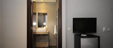 A hotel room with a television on a small table, a bathroom with a sink and mirror, and a door leading to another room.