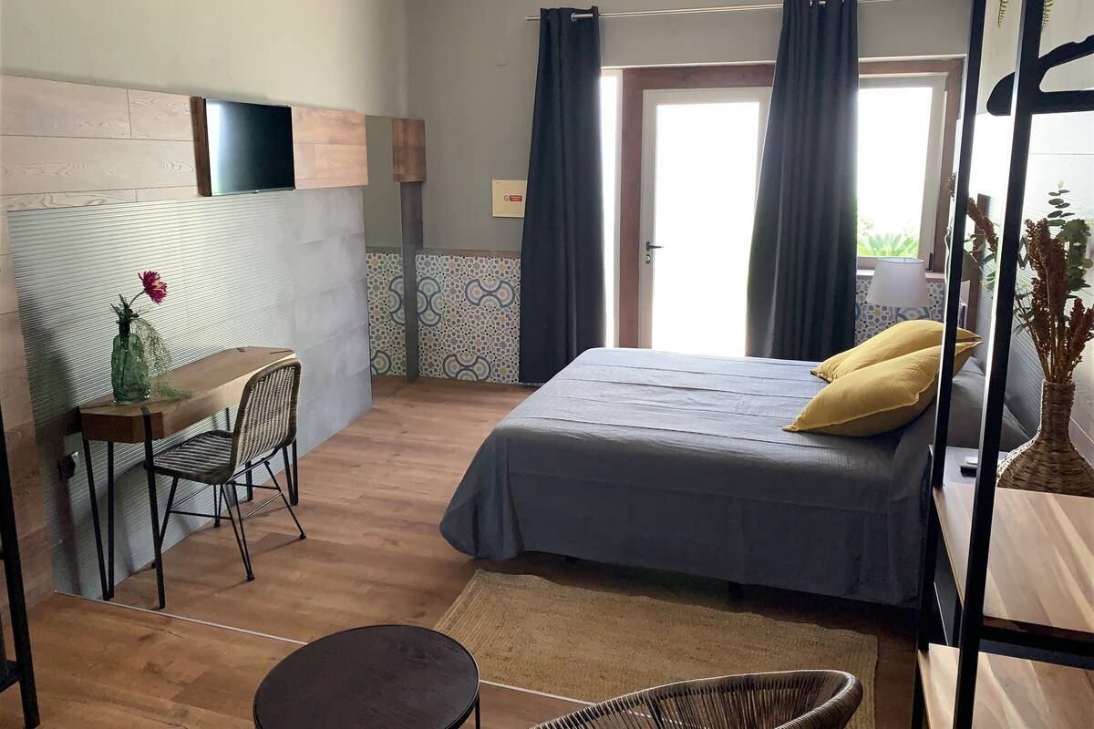 A room with a bed, a desk, a chair, and a small table with a vase.