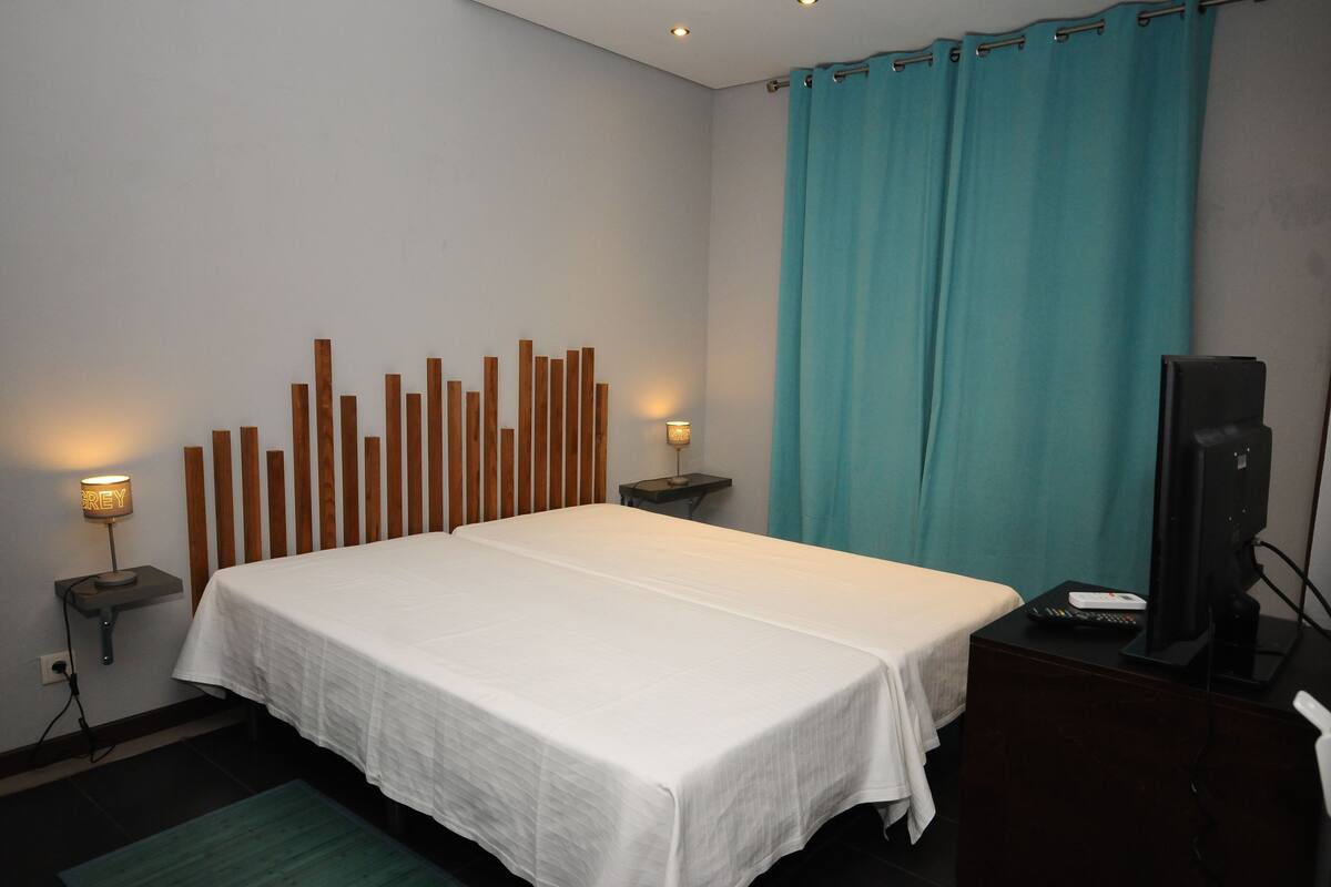 A hotel room with a large bed, two bedside tables with lamps, a television, and a curtain.