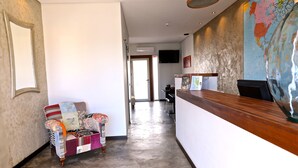 A hotel lobby with a wooden reception desk, a patterned armchair, and a large world map on the wall. - Lost & Found - Guesthouse & Suites (Albufeira)