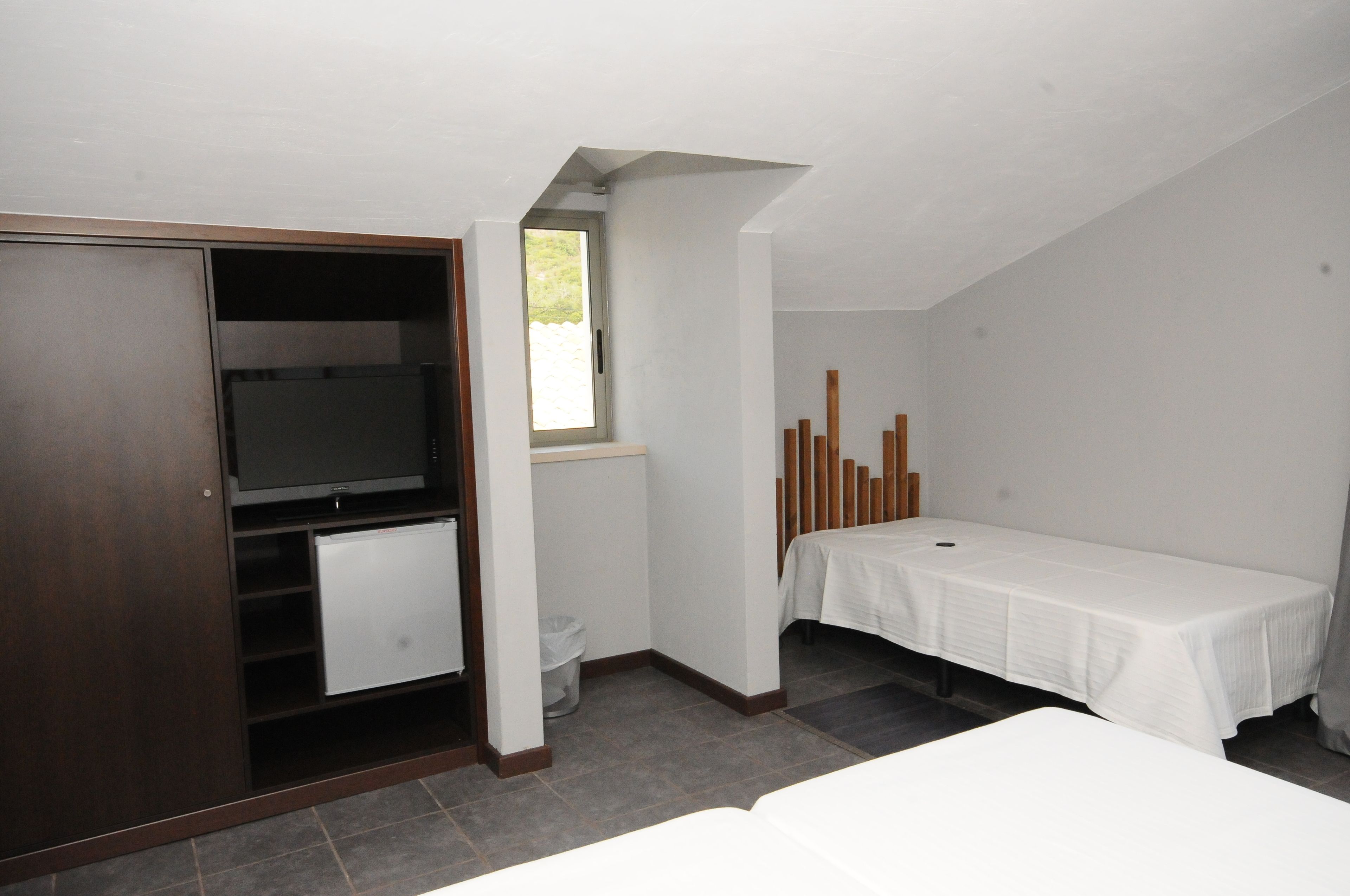 Ein kleiner, einfach eingerichteter Raum mit einem Bett, einem Schreibtisch, einem Kleiderschrank und einem Fenster.
