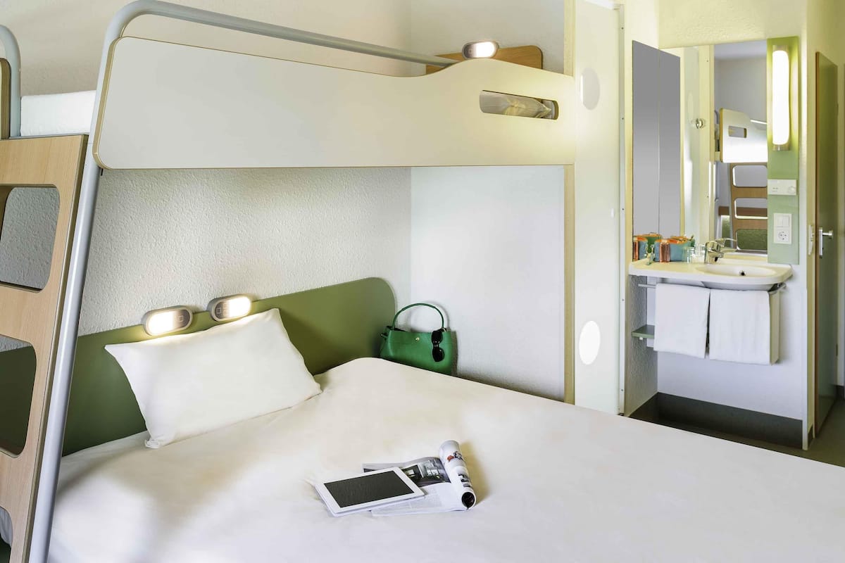Un lit superposé avec une table de chevet, un sac vert et un magazine sur le lit.