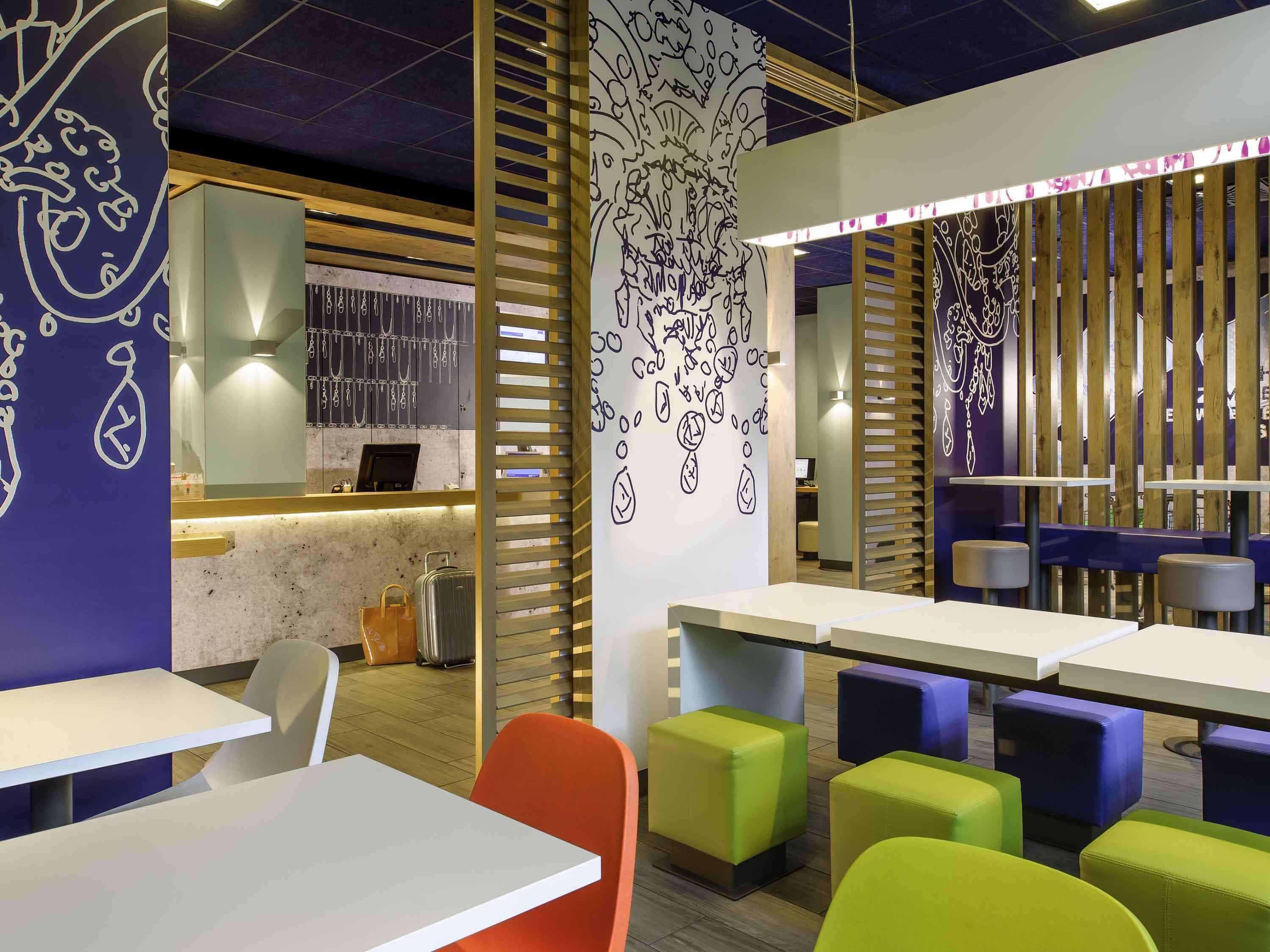Ein modernes Restaurantambiente mit weißen Tischen, bunten Hocker und Wanddekoration.