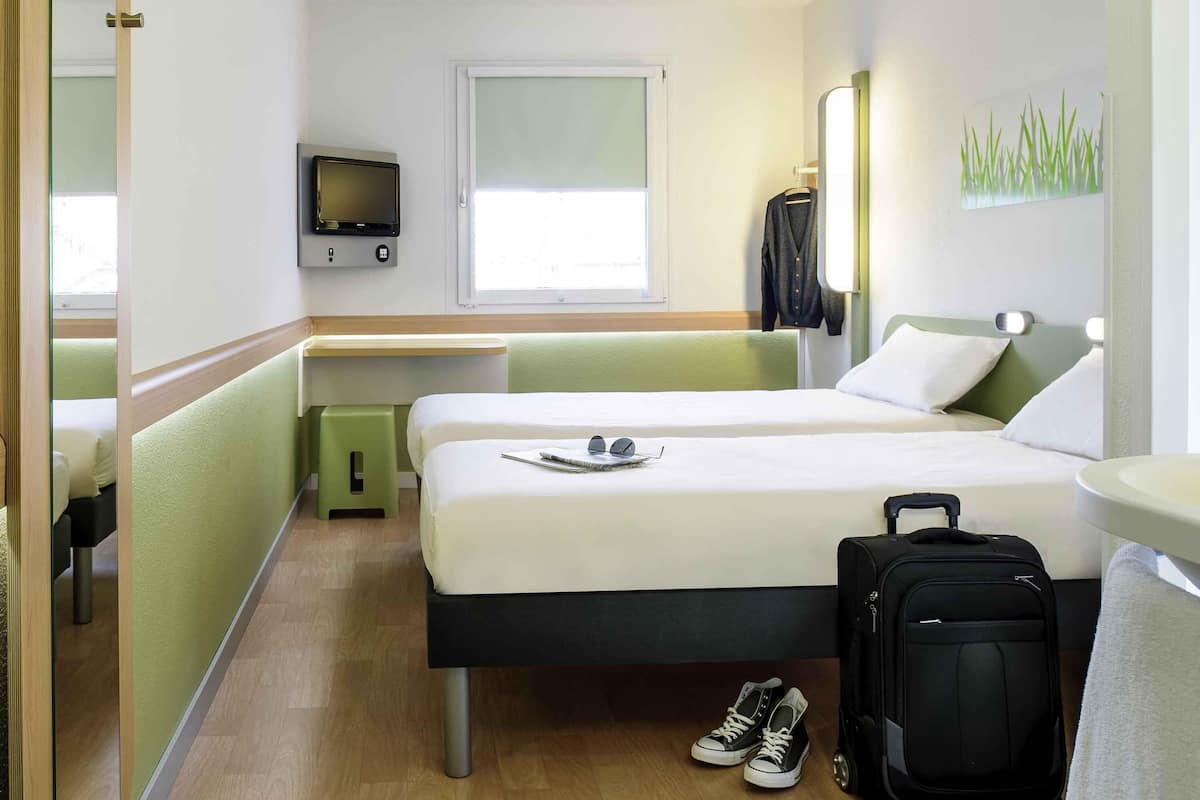 Une chambre d’hôtel avec deux lits, une télévision, une fenêtre, un bureau et une valise.