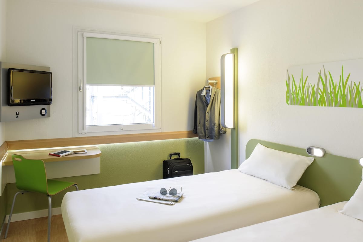 Ein Hotelzimmer mit Bett, Schreibtisch, Sessel, Fernseher und Fenster.