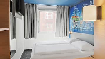 Quarto de hotel com cama, cortinas, janela, luminária na parede e um mural com vista para a cidade.