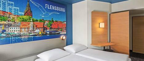 Habitación de hotel con cama, mesita de noche, lámpara de pared y un mural con vista a la ciudad.