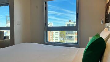 Una habitación de hotel con un ventanal grande, una cama y vistas a edificios.