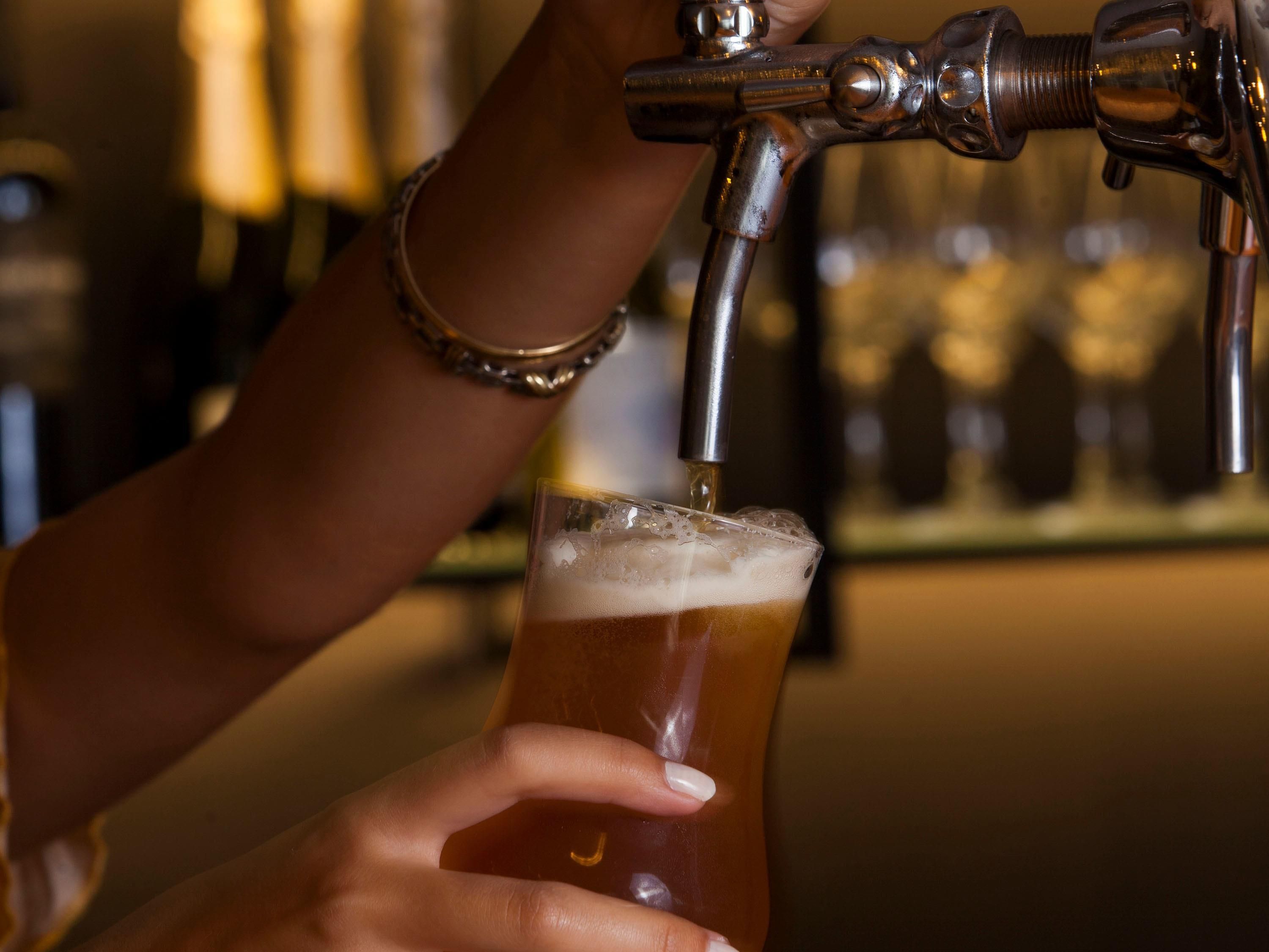 A hand holding a glass of beer being filled from a tap.