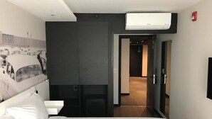 A modern hotel room with a large bed, a wall-mounted air conditioner, a door leading to a hallway, and a small desk with a chair. - ibis styles Montevideo Biarritz Hotel (Montevideo)