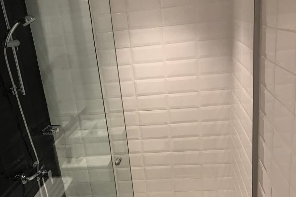 Una ducha con paredes de vidrio, azulejos blancos y una pared con revestimiento negro.