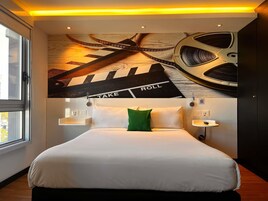 Habitación de hotel con una cama, un almohadón verde, un reloj en la pared y un techo con diseño de celuloide.